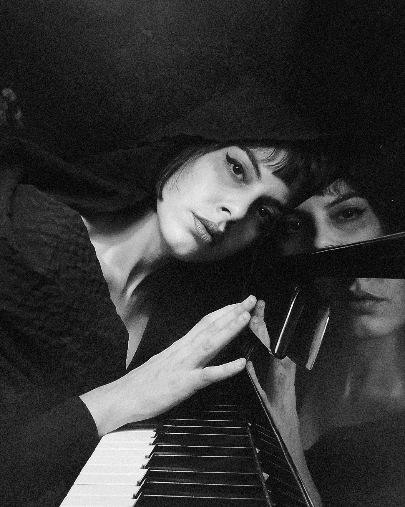 Black and white photo of Neoclassical artist Antinoë playing a piano with a mirror reflection.